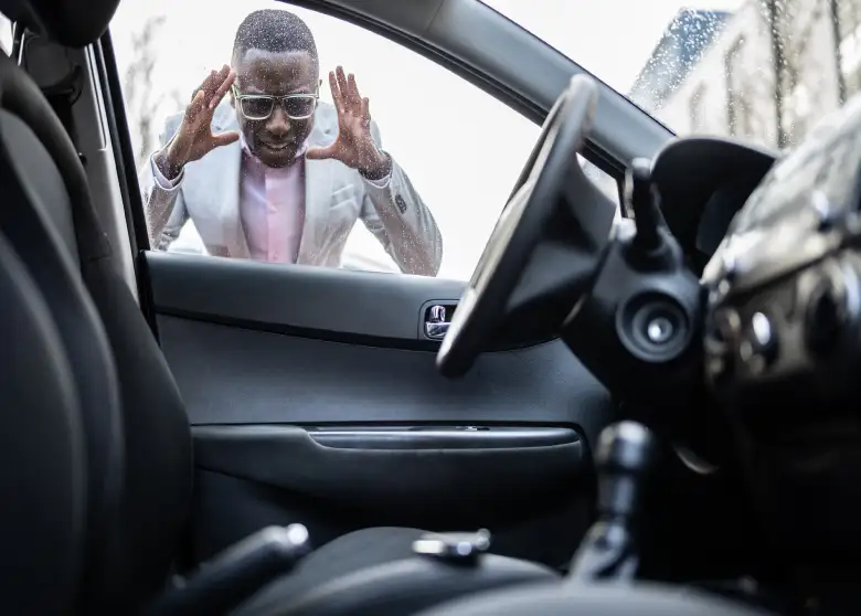 Frustrated man in a gray blazer looking through a car window after locking his keys inside the vehicle